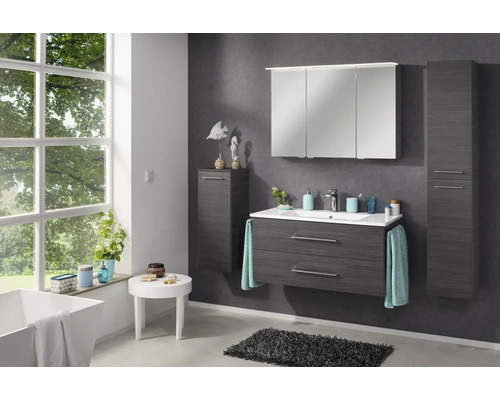 Modernes, helles Badezimmer mit Badmöbelset in Anthrazit-Holzoptik, Keramikwaschbecken, Spiegelschrank und Schränken neben einem Fenster.