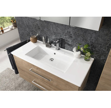 Meuble de lavabo moderne avec vasque blanche, robinetterie chromée et meuble bas en aspect bois devant un mur à motifs.