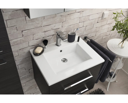 Meuble de salle de bain moderne avec vasque en céramique blanche, robinetterie chromée et meuble foncé contre un mur aspect pierre.