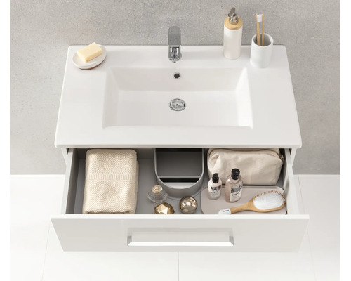 Meuble sous-vasque blanc moderne avec lavabo en céramique et un tiroir ouvert montrant un rangement organisé pour les articles de toilette.