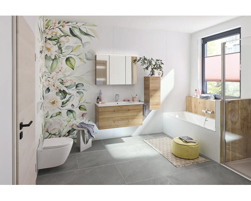 Salle de bains moderne et lumineuse avec meuble sous-lavabo aspect bois, armoire de toilette, baignoire blanche et papier peint floral.
