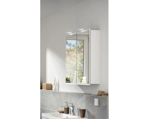 Armoire de toilette moderne à deux portes avec éclairage LED au-dessus d'un lavabo dans une salle de bains lumineuse avec carrelage mural.