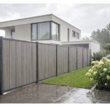 Clôture pare-vue moderne composée de panneaux verticaux en matériau composite sous la pluie dans un jardin avec pelouse.