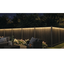 Clôture de jardin éclairée de nuit avec ruban LED, mobilier de jardin et fleurs.