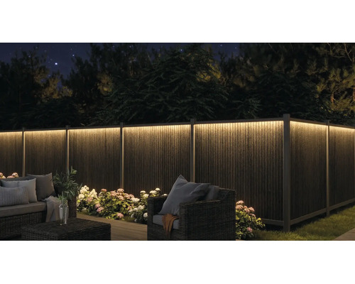 Clôture de jardin éclairée de nuit avec ruban LED, mobilier de jardin et fleurs.