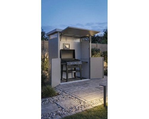 Armoire de barbecue en métal avec toit ouvrant et portes, contenant un barbecue à gaz Tenneker sur une terrasse pavée dans un jardin au crépuscule.