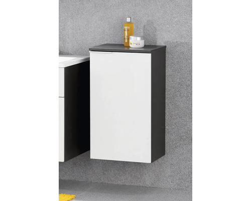 Meuble latéral de salle de bains suspendu avec porte blanche et corps anthracite portant des articles de toilette.