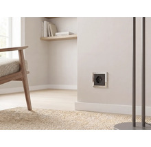 Schukosteckdose mit silbernem Rahmen und schwarzem Einsatz an einer hellen Wand in einem modernen Wohnzimmer.