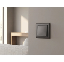 Interrupteur anthracite sur un mur gris dans un salon moderne avec canapé et table en bois.