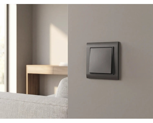Interrupteur anthracite sur un mur gris dans un salon moderne avec canapé et table en bois.