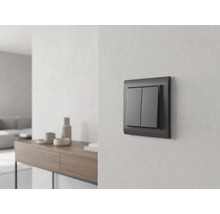 Anthrazitfarbener Serienschalter an einer hellen Wand in einem hellen, modern eingerichteten Wohnraum mit Sideboard im Hintergrund.