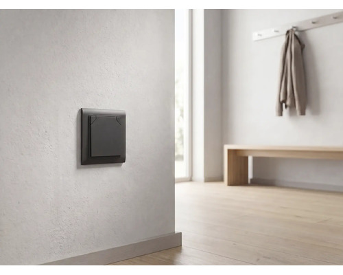 Interrupteur moderne gris foncé sur un mur clair dans un couloir lumineux et minimaliste avec un sol en bois.