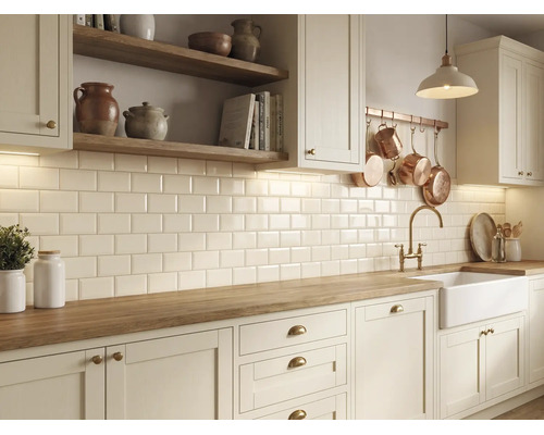 Helle Küche im Landhausstil mit Holz-Arbeitsplatte, weißen Metrofliesen und weißem Spülstein mit goldener Armatur.