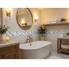 Modernes, helles Badezimmer mit freistehender Badewanne, rundem Spiegel, Holzmöbeln, Metrofliesen und dekorativer Mosaikbordüre.