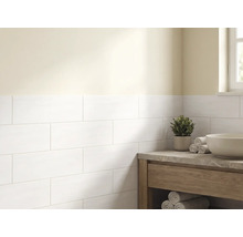 Salle de bains lumineuse avec des carreaux de mur blancs rectangulaires posés en décalé et un meuble sous-vasque en bois avec plan en pierre.