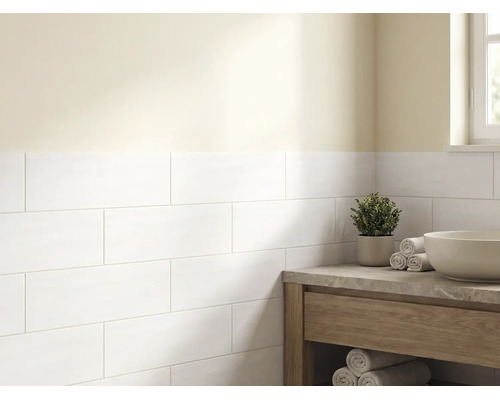 Salle de bains lumineuse avec des carreaux de mur blancs rectangulaires posés en décalé et un meuble sous-vasque en bois avec plan en pierre.