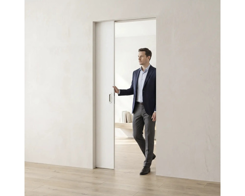 Ein Mann im Anzug öffnet eine weiße, minimalistische Schiebetür in einem hellen, modern gestalteten Raum mit Holzfußboden.