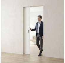Ein Mann im Anzug öffnet eine weiße, minimalistische Schiebetür in einem hellen, modern gestalteten Raum mit Holzfußboden.