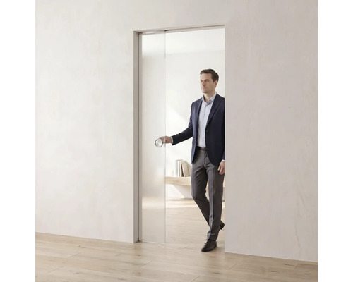 Porte coulissante en verre dans une pièce lumineuse et minimaliste avec une personne utilisant la poignée de porte ronde.