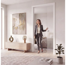 Porte coulissante moderne en verre dans un intérieur lumineux, design sans cadre avec poignée ronde, femme passant par la porte ouverte.