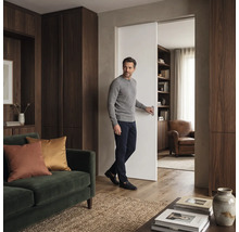 Ein Mann öffnet eine Schiebetür in einem modern eingerichteten Wohnzimmer mit Holzschränken und einem Sofa.