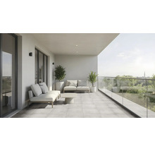 Moderner, großzügiger Balkon mit Loungemöbeln, Couchtisch, gefliestem Boden und Glasgeländer mit Blick in die Natur.