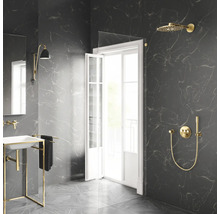 Salle de bains moderne avec carrelage en marbre foncé, robinetterie de douche dorée, paroi en verre et lavabo blanc sur cadre doré.
