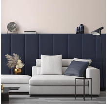 Modernes Wohnzimmer mit dunkelblauen gepolsterten Wandpaneelen, einem hellgrauen Sofa mit Kissen, einem schwarzen Beistelltisch und einer Stehlampe.
