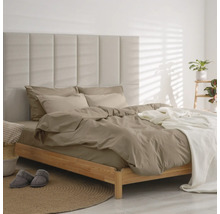 Modernes Schlafzimmer mit Holzbett, gepolstertem Paneel-Kopfteil, taupefarbener Bettwäsche und weißem Überwurf auf einem runden Jute-Teppich.