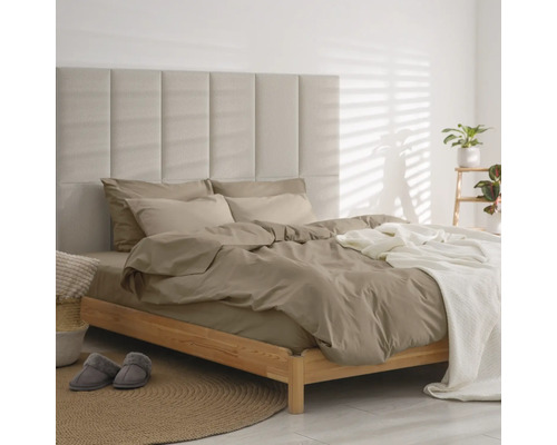 Modernes Schlafzimmer mit Holzbett, gepolstertem Paneel-Kopfteil, taupefarbener Bettwäsche und weißem Überwurf auf einem runden Jute-Teppich.