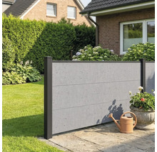 Moderner Sichtschutzzaun in Beton-Optik mit dunklen Pfosten in einem Garten auf einer Steinterrasse neben einer Gießkanne.