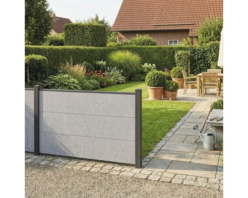 Moderner Sichtschutzzaun in Betonoptik im Garten mit Rasen, Beeten und einer gepflasterten Terrasse mit Holzmöbeln.