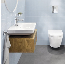Salle de bains moderne et lumineuse avec lavabo en céramique sur meuble en bois, robinetterie chromée et WC suspendu sur murs carrelés.
