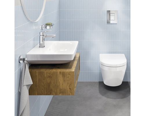 Salle de bains moderne et lumineuse avec lavabo en céramique sur meuble en bois, robinetterie chromée et WC suspendu sur murs carrelés.