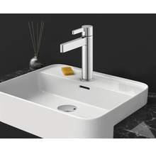 Mitigeur de lavabo monocommande moderne en chrome sur un lavabo en céramique blanc avec un savon sur un plan de travail en marbre.