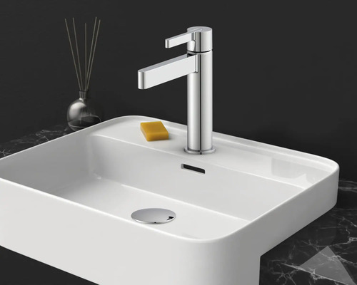 Mitigeur de lavabo monocommande moderne en chrome sur un lavabo en céramique blanc avec un savon sur un plan de travail en marbre.