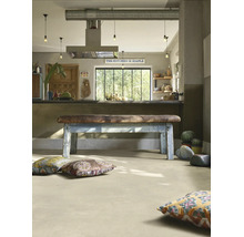 Cuisine industrielle avec sol clair aspect béton, banc vintage en cuir et bois et coussins de sol colorés.