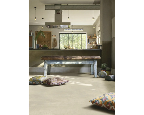 Cuisine industrielle avec sol clair aspect béton, banc vintage en cuir et bois et coussins de sol colorés.