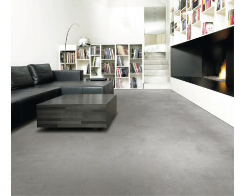 Salon moderne avec revêtement de sol gris aspect béton, canapé en cuir noir, table basse foncée et cheminée minimaliste.