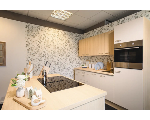 Cuisine moderne et lumineuse avec un îlot central équipé d'une plaque de cuisson noire, meubles hauts en bois clair et papier peint floral.
