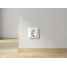 Prise de courant sur un mur blanc au-dessus d'une plinthe en bois clair dans une pièce lumineuse.