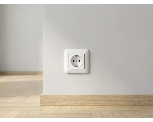 Prise de courant sur un mur blanc au-dessus d'une plinthe en bois clair dans une pièce lumineuse.