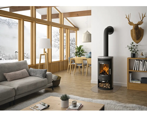 Poêle à bois moderne en acier avec vitre dans un salon lumineux avec de grandes fenêtres et vue sur un paysage enneigé.