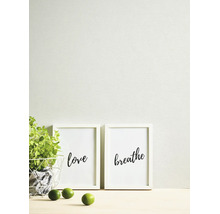 Scène lumineuse et organisée avec papier peint texturé, deux cadres blancs avec les mots love et breathe, une plante verte et des citrons verts.