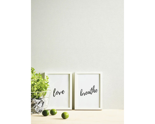 Scène lumineuse et organisée avec papier peint texturé, deux cadres blancs avec les mots love et breathe, une plante verte et des citrons verts.