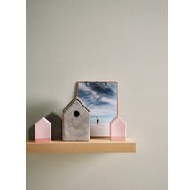 Papier peint intissé structuré vert clair sur un mur derrière une étagère en bois avec des objets de décoration comme des petites maisons.