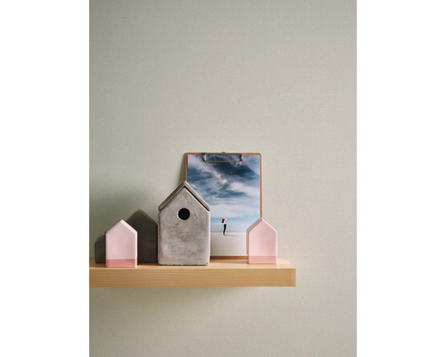 Papier peint intissé structuré vert clair sur un mur derrière une étagère en bois avec des objets de décoration comme des petites maisons.