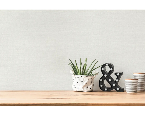 Papier peint structuré sur un mur derrière une table en bois avec une plante et des objets de décoration.