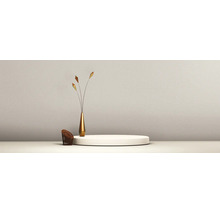 Scène minimaliste lumineuse avec socle blanc, vase doré avec branches décoratives et petit panier devant un mur structuré.