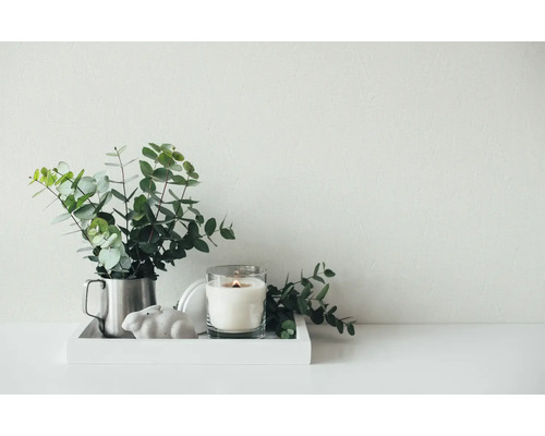 Composition décorative sur un plateau avec des branches d'eucalyptus dans un gobelet en métal, une bougie allumée dans un verre et un petit lapin.